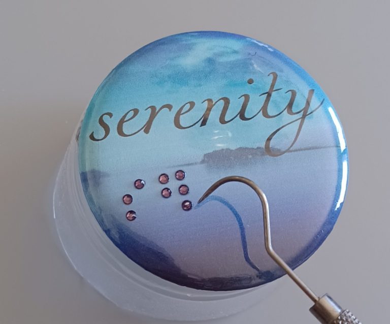 2.25 round pin back button, black print and raised braille dots reading serenity